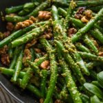 Close up angled view of a small cast iron skillet filled with pesto green beans with toasted walnuts and lemon zest.