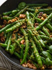 Close up angled view of a small cast iron skillet filled with pesto green beans with toasted walnuts and lemon zest.