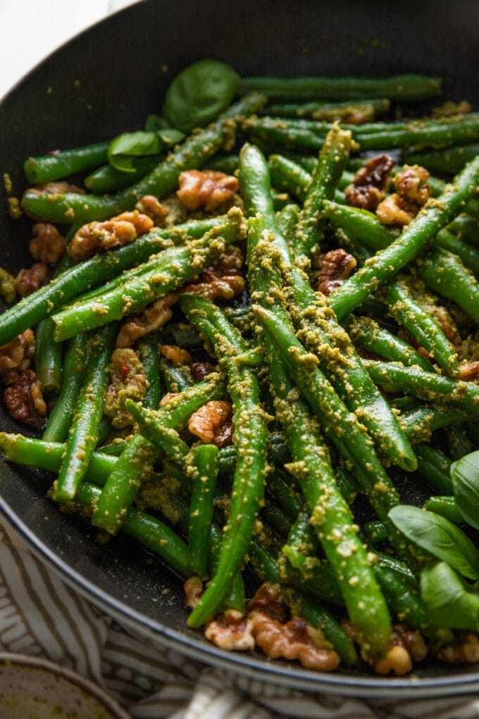 Close up angled view of a small cast iron skillet filled with pesto green beans with toasted walnuts and lemon zest.