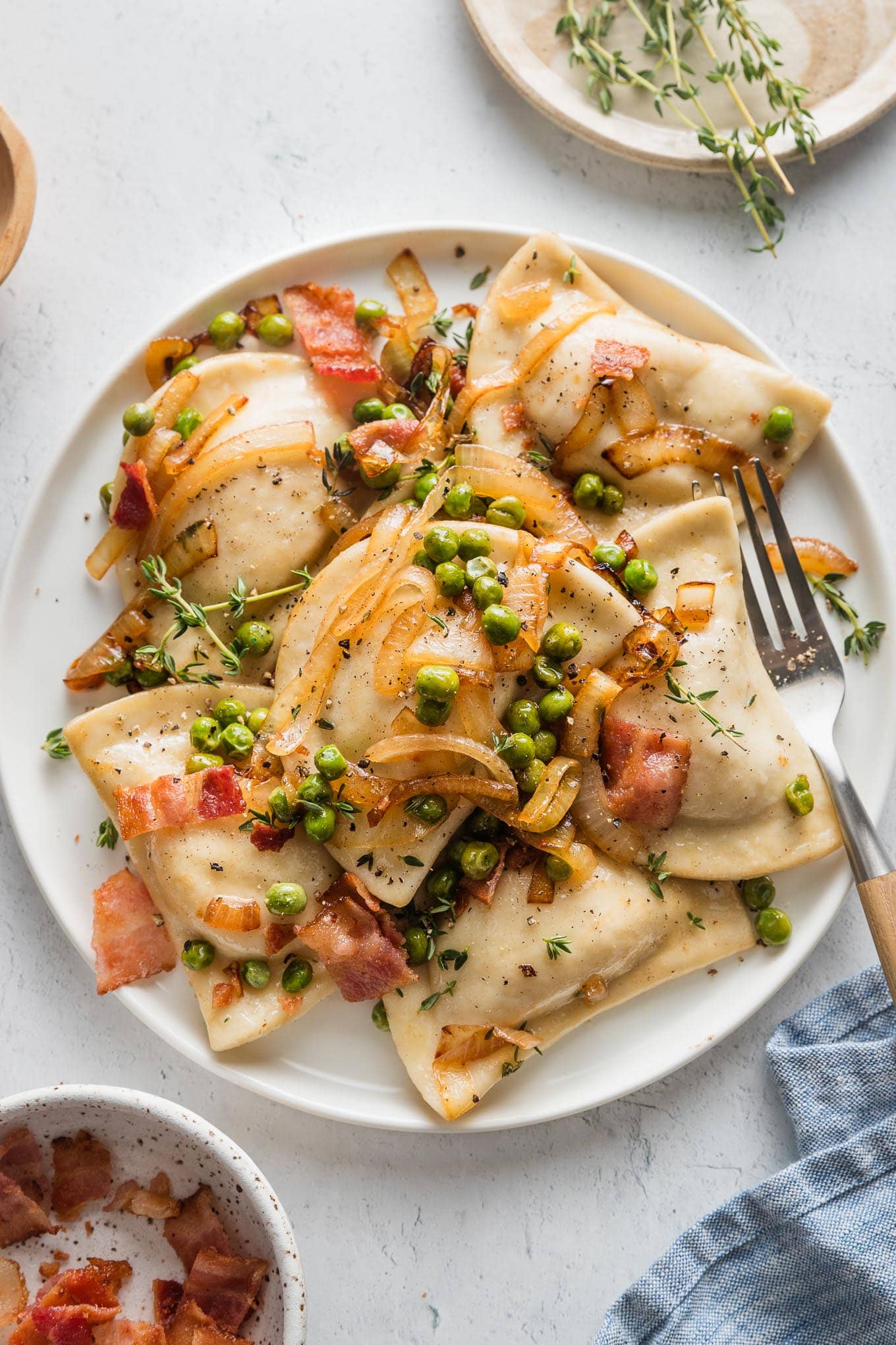 Small white plate filled with cheddar pierogies in a sauce of butter, caramelized onions, bacon, and peas.