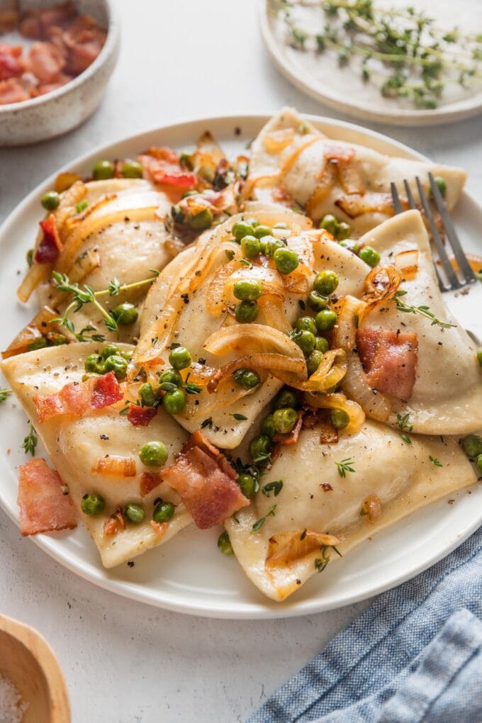 Angled view of a small plate with a generous serving of pierogies with bacon, onions, and peas.
