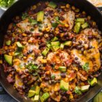 Large, deep cast iron skillet full of a Santa Fe chicken dish with black beans, corn, and salsa.