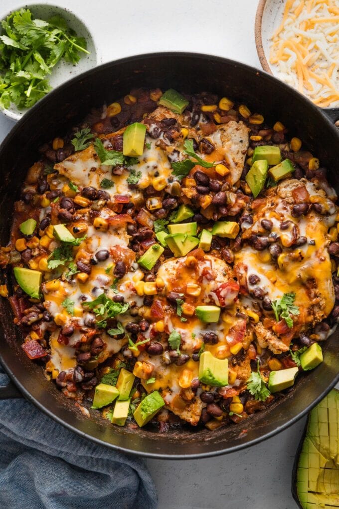 Large, deep cast iron skillet full of a Santa Fe chicken dish with black beans, corn, and salsa.