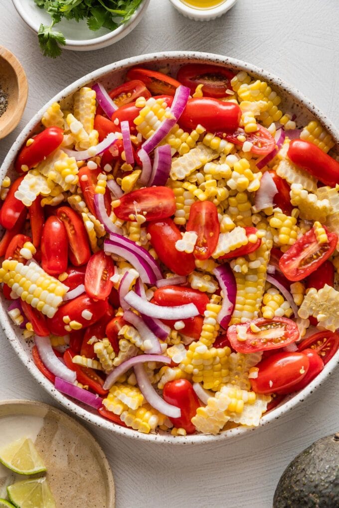 Corn kernels, halved cherry tomatoes, and thinly sliced red onion tossed together in a large low bowl.