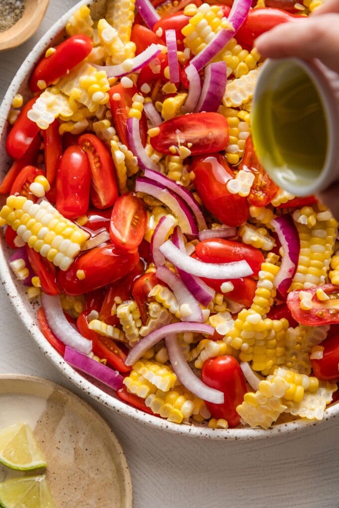 Olive oil being poured over a corn and cherry tomato salad mix.