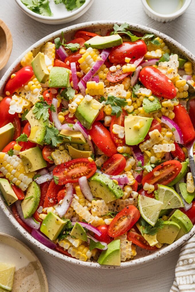 Low white bowl filled with corn avocado tomato salad with red onion and cilantro.