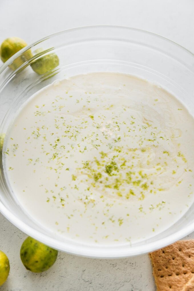 A mixture of sweetened condensed milk and cream in a large bowl, with visible lime zest sprinkled on top.