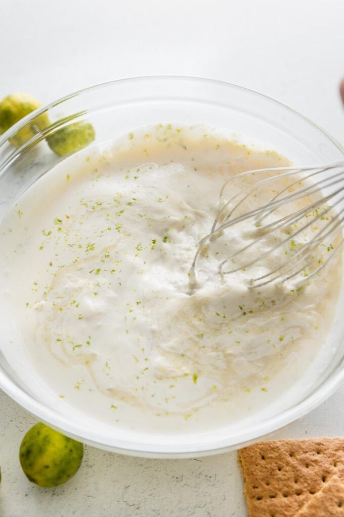 Action shot of a large metal whisk incorporating lime juice and zest into a cream mixture.