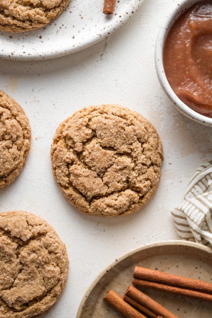 Overhead view of a crackly-topped apple butter snickerdoodle resting alone on a countertop with cinnamon sticks scattered nearby.