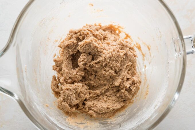 Overhead view of a clear glass stand mixer bowl holding dough for apple butter snickerdoodles.