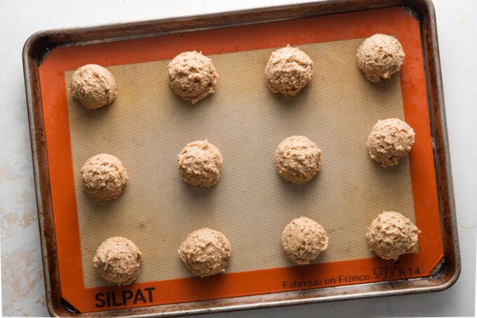 Scooped dough balls for apple butter snickerdoodles arranged on a large baking sheet lined with a silicone baking mat, not yet rolled in cinnamon sugar.
