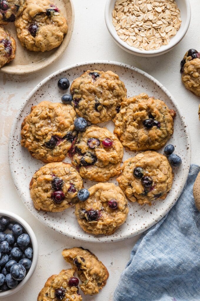 Countertop scattered with blueberry oatmeal cookies, extra blueberries, extra oats, and sea salt.