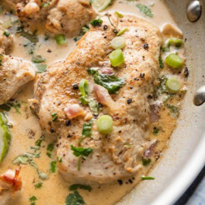 Close up of a chicken breast in creamy cilantro lime sauce with red onions and green onions for garnish.