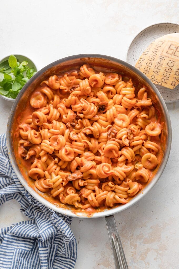 Overhead view of a large skillet full of creamy tomato pasta with sun-dried tomatoes mixed in.