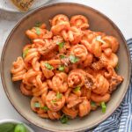 Low ceramic bowl with a large helping of creamy sun-dried tomato pasta garnished with fresh basil and Parmesan.