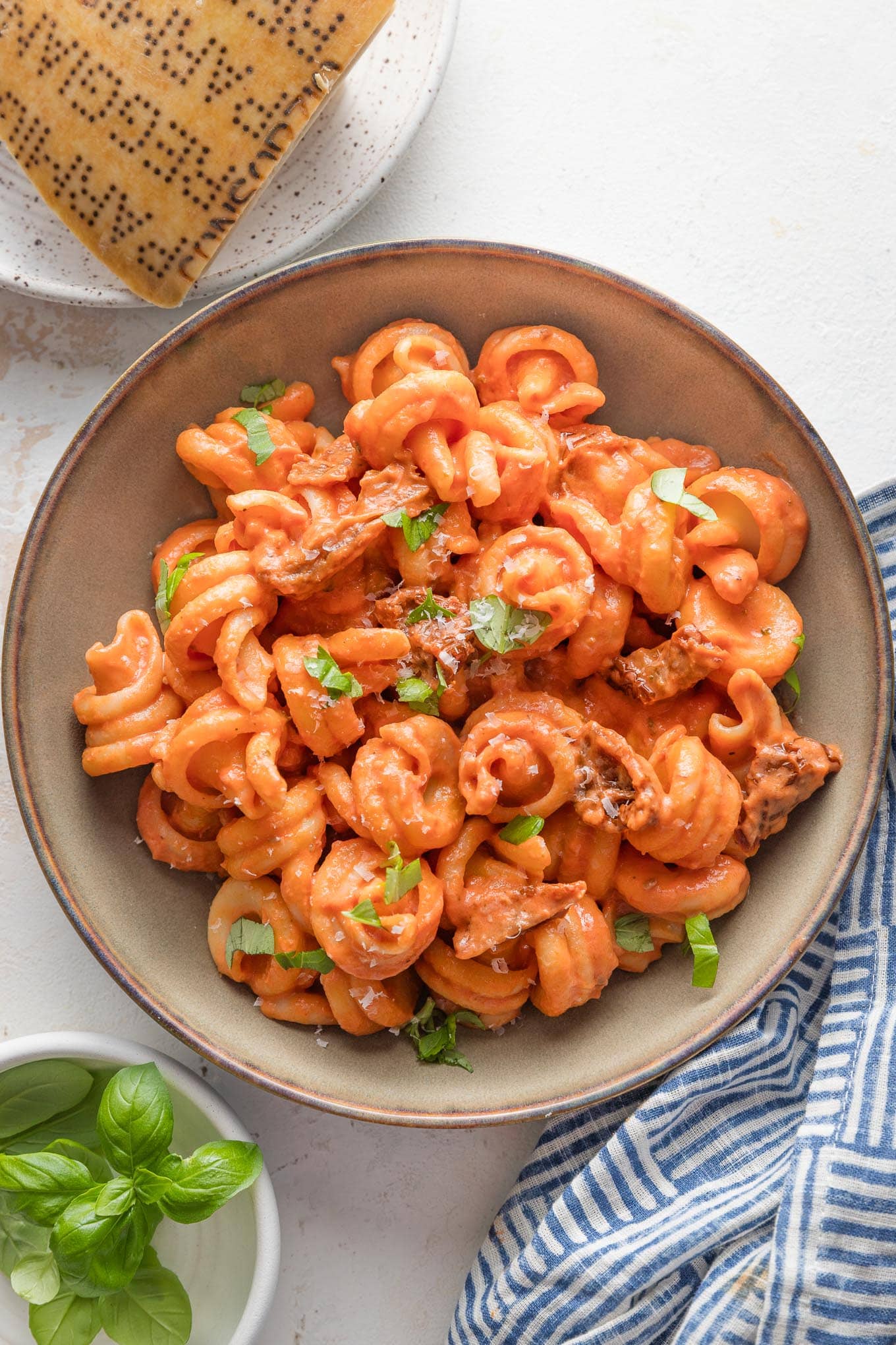 Low ceramic bowl with a large helping of creamy sun-dried tomato pasta garnished with fresh basil and Parmesan.