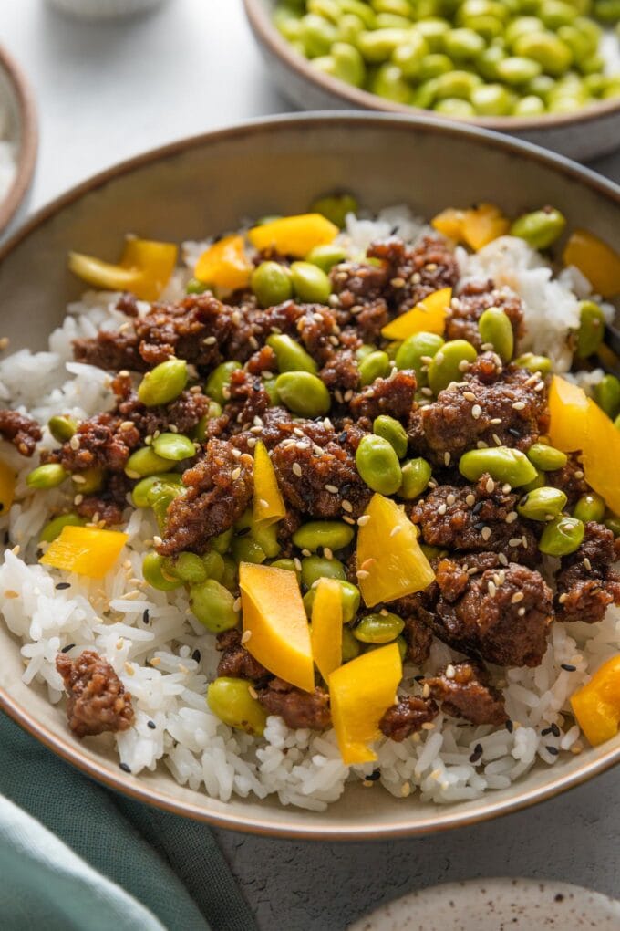 Angled view of edamame ground beef bowls served with extra shelled edamame on the side.