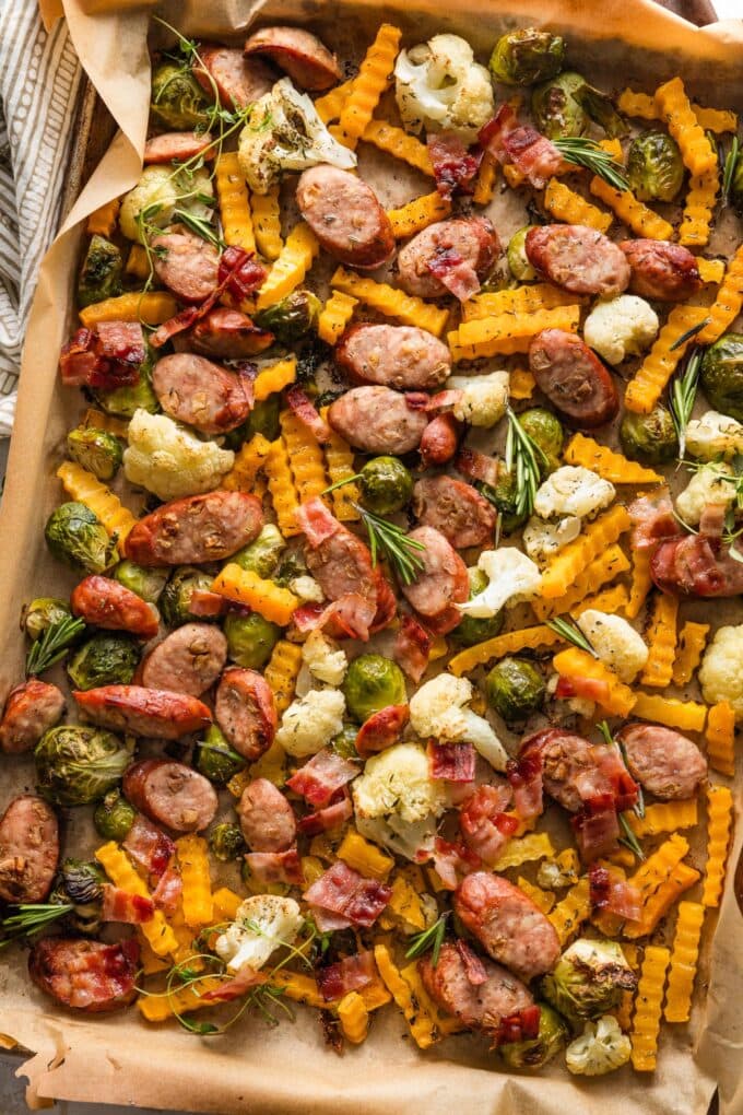 Sheet pan filled with roasted apple chicken sausage, butternut squash, Brussels sprouts, and cauliflower, tossed with rosemary and sage.