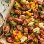 Close up of a lined sheet pan filled with apple chicken sausage and fall veggies, including Brussels sprouts, cauliflower, and butternut squash.