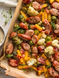 Close up of a lined sheet pan filled with apple chicken sausage and fall veggies, including Brussels sprouts, cauliflower, and butternut squash.