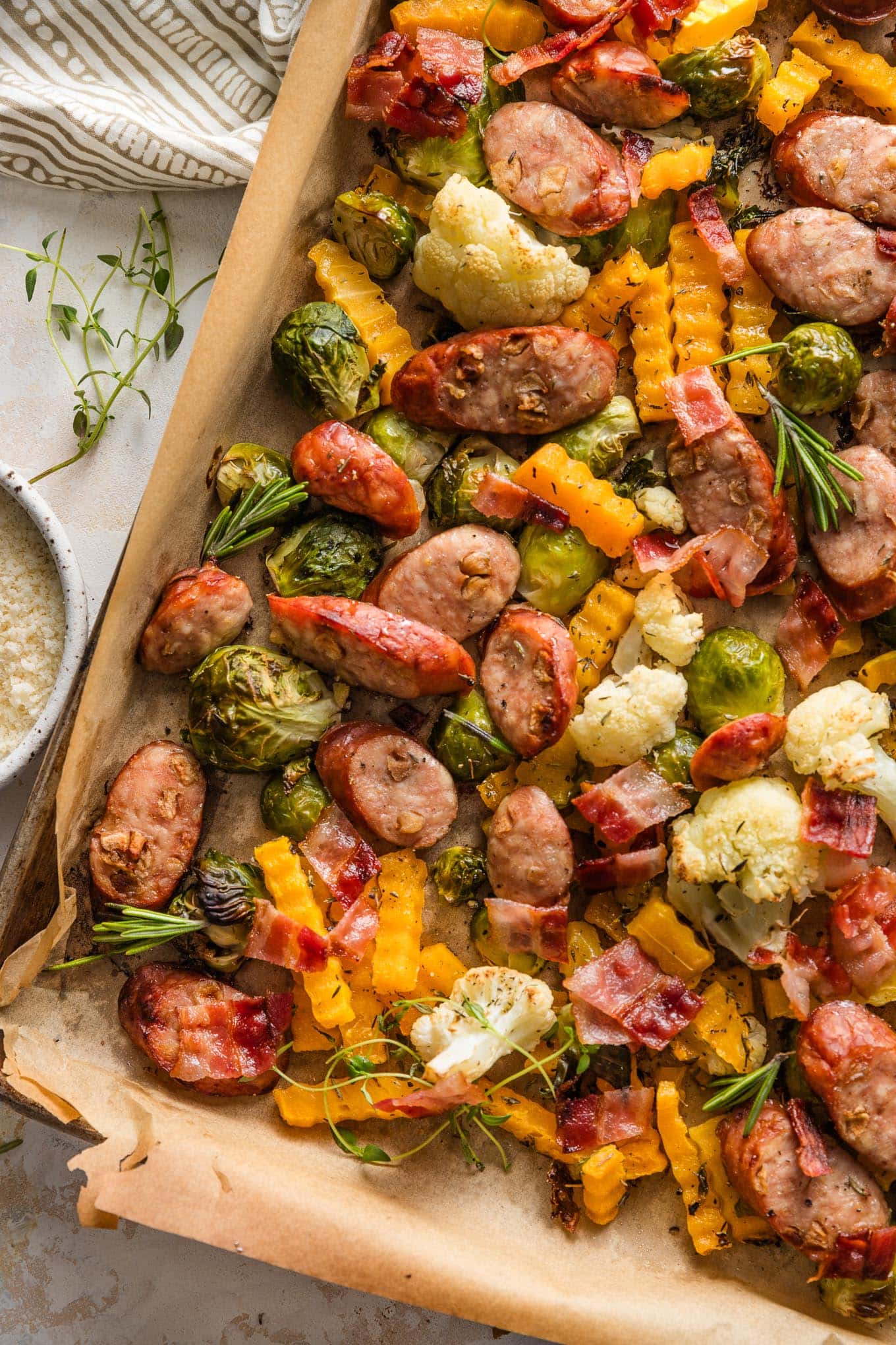 Close up of a lined sheet pan filled with apple chicken sausage and fall veggies, including Brussels sprouts, cauliflower, and butternut squash.