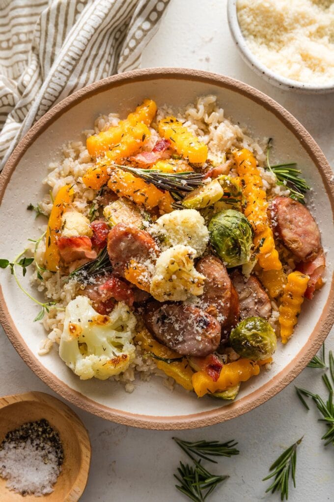 Bowl filled with brown rice and a harvest sheet pan dinner of chicken sausage and veggies.