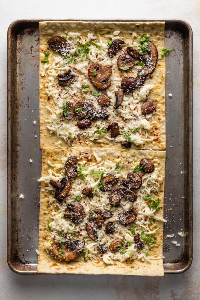 Large baking tray with two mushroom flatbreads, ready to go into the oven.