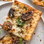 Close up of a crisp mushroom flatbread made on lavash, with Parmesan and mozzarella cheese, fresh basil, and red pepper flakes.