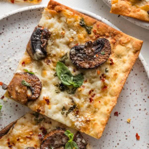 Close up of a crisp mushroom flatbread made on lavash, with Parmesan and mozzarella cheese, fresh basil, and red pepper flakes.