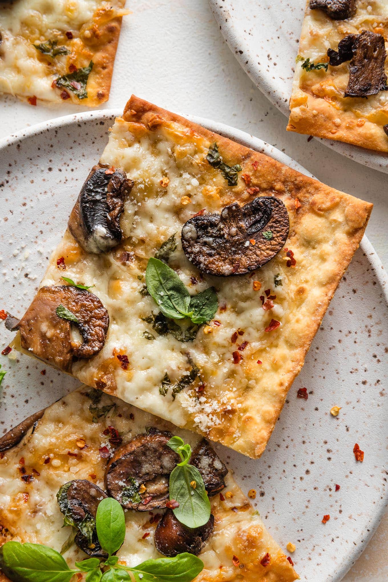 Close up of a crisp mushroom flatbread made on lavash, with Parmesan and mozzarella cheese, fresh basil, and red pepper flakes.