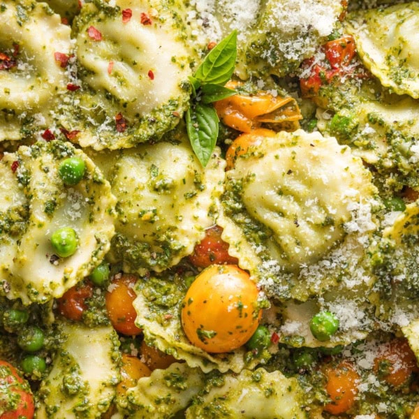 Close up of ravioli with a simple pesto sauce, burst cherry tomatoes, and tender peas.