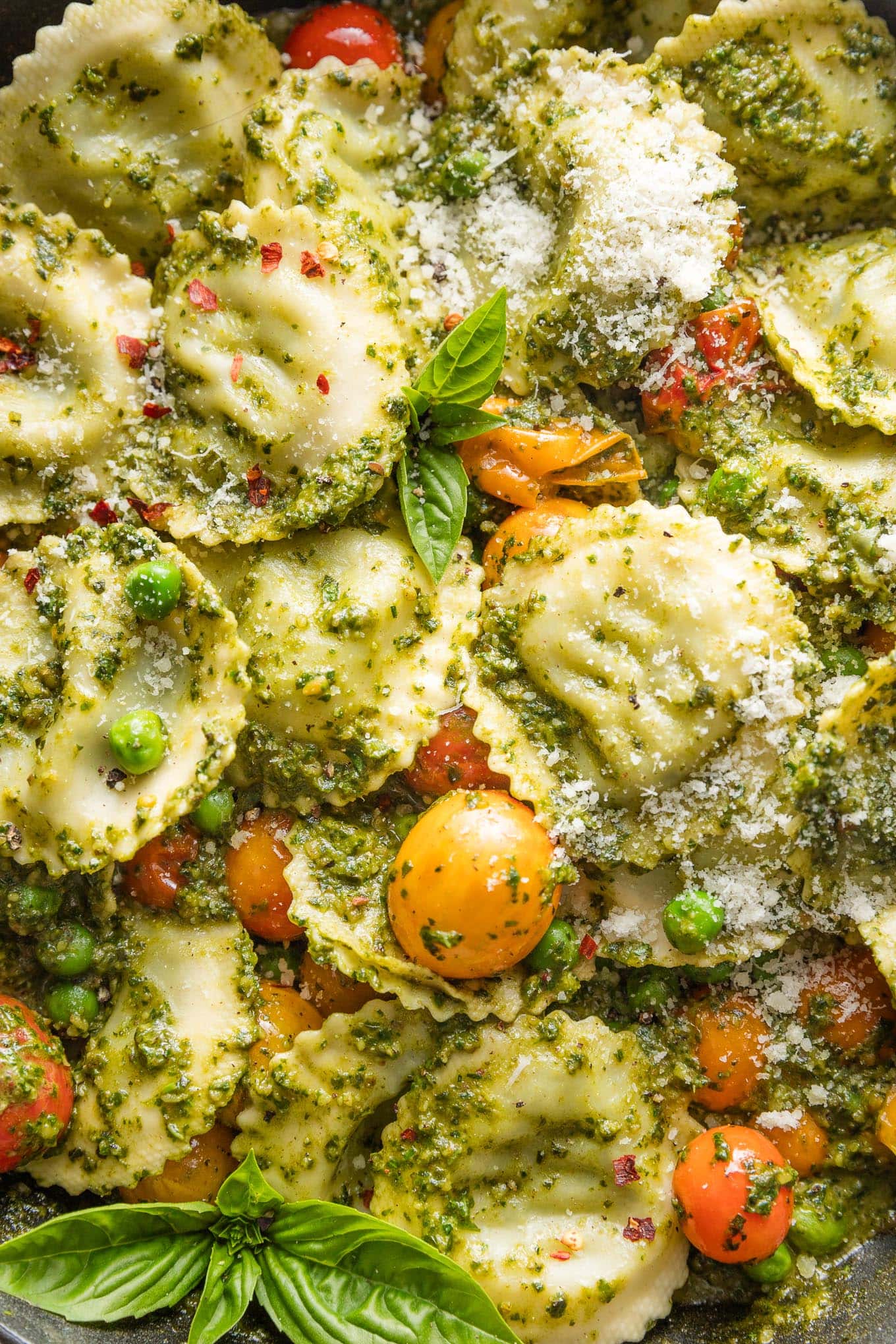 Close up of ravioli with a simple pesto sauce, burst cherry tomatoes, and tender peas.