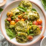 Small pasta bowl filled with pesto ravioli with peas and cherry tomatoes, with extra red pepper flakes nearby for garnish.