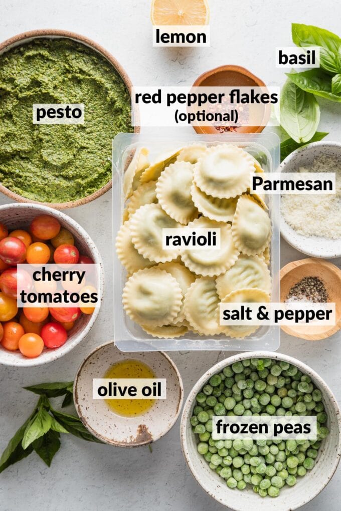 Labeled overhead photo of ravioli, pesto, cherry tomatoes, frozen peas, red pepper flakes, extra basil, olive oil, Parmesan, lemon, salt, and pepper, all in prep bowls and ready to cook.