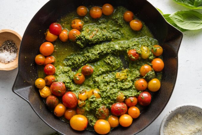 Pesto mixed into cherry tomatoes in a skillet.