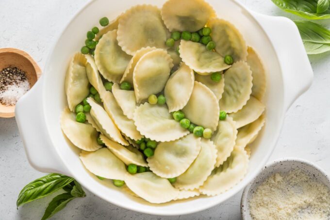 Cooked ravioli and peas drained together in a simple white colander.