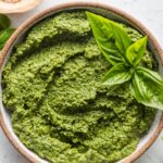 Small bowl full of homemade spinach pesto with a basil leaf on top for garnish.