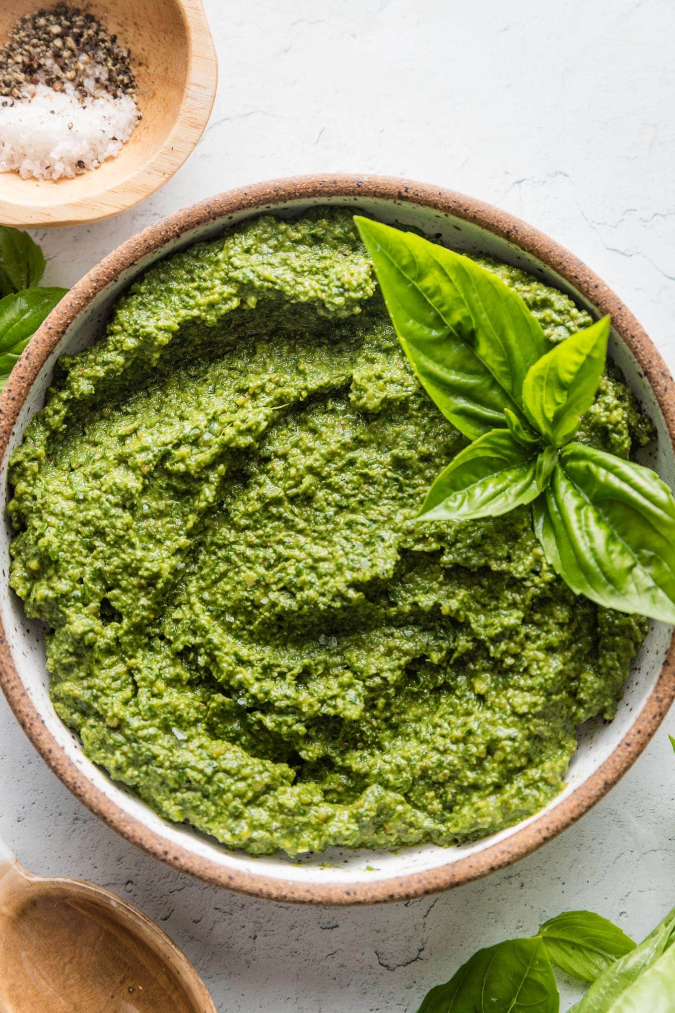 Small bowl full of homemade spinach pesto with a basil leaf on top for garnish.