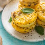Close up of high protein sausage cheddar egg bites with cottage cheese piled on a plate and garnished with leaves of fresh basil.