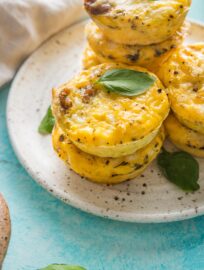 Close up of high protein sausage cheddar egg bites with cottage cheese piled on a plate and garnished with leaves of fresh basil.