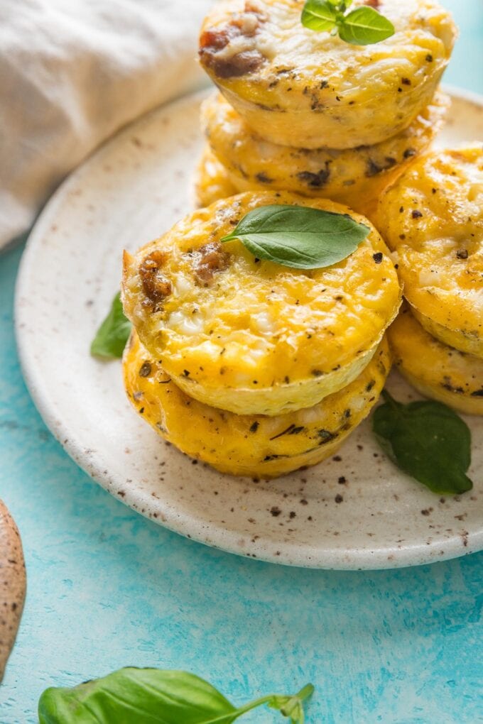 Close up of high protein sausage cheddar egg bites with cottage cheese piled on a plate and garnished with leaves of fresh basil.