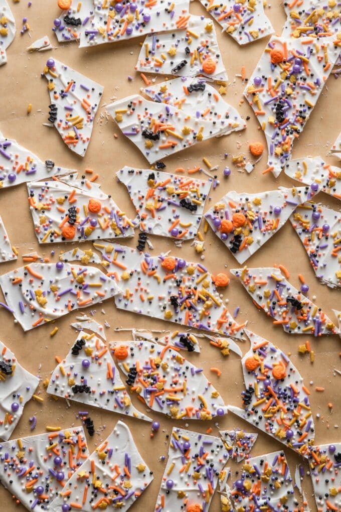 Piece of brown parchment paper scattered with broken pieces of "boo bark" -- in this example, white chocolate spread into a thin layer and topped with bat- and ghost-themed sprinkles for a Halloween treat.