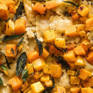 Close up view of cheese ravioli with brown butter sauce, sage, lemon juice, and cubed butternut squash.