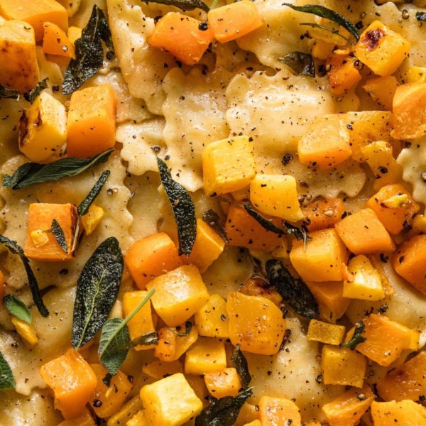 Close up view of cheese ravioli with brown butter sauce, sage, lemon juice, and cubed butternut squash.