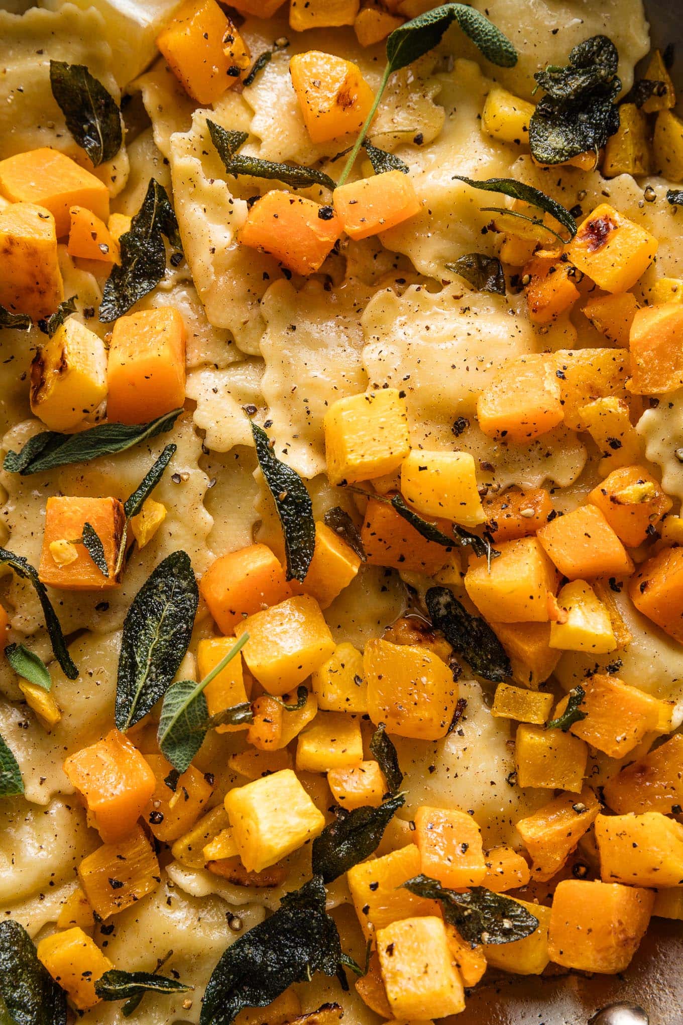 Close up view of cheese ravioli with brown butter sauce, sage, lemon juice, and cubed butternut squash.