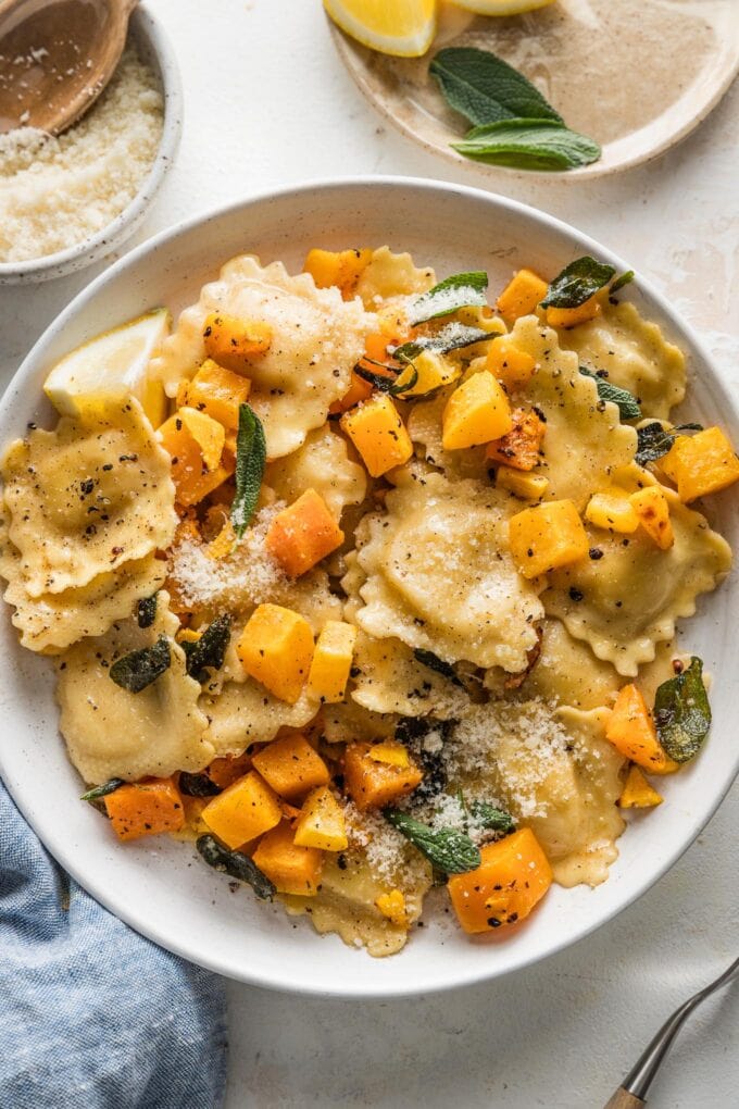 Low pasta bowl full of ravioli with brown butter sauce, butternut squash, sage, and Parmesan.