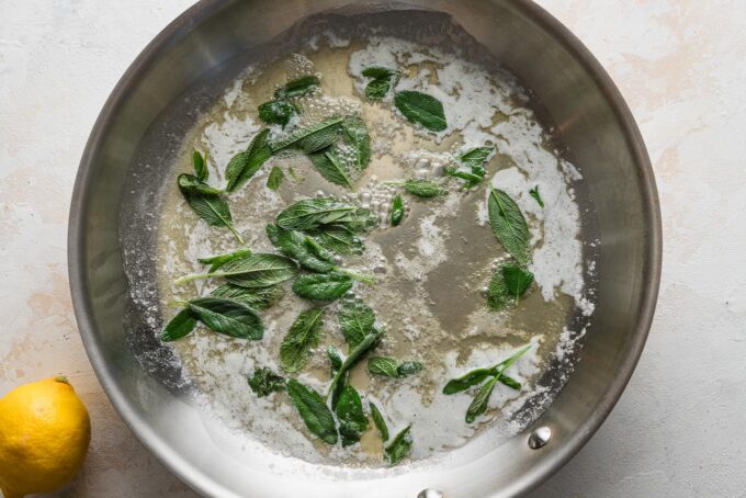 Melted butter in a skillet with sage leaves simmering inside.