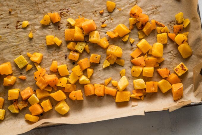 Butternut squash cubes roasted on a large, parchment-lined baking sheet.