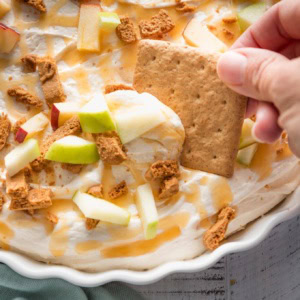 Close up of a graham cracker being swooped through a dish of caramel apple cheesecake dip.