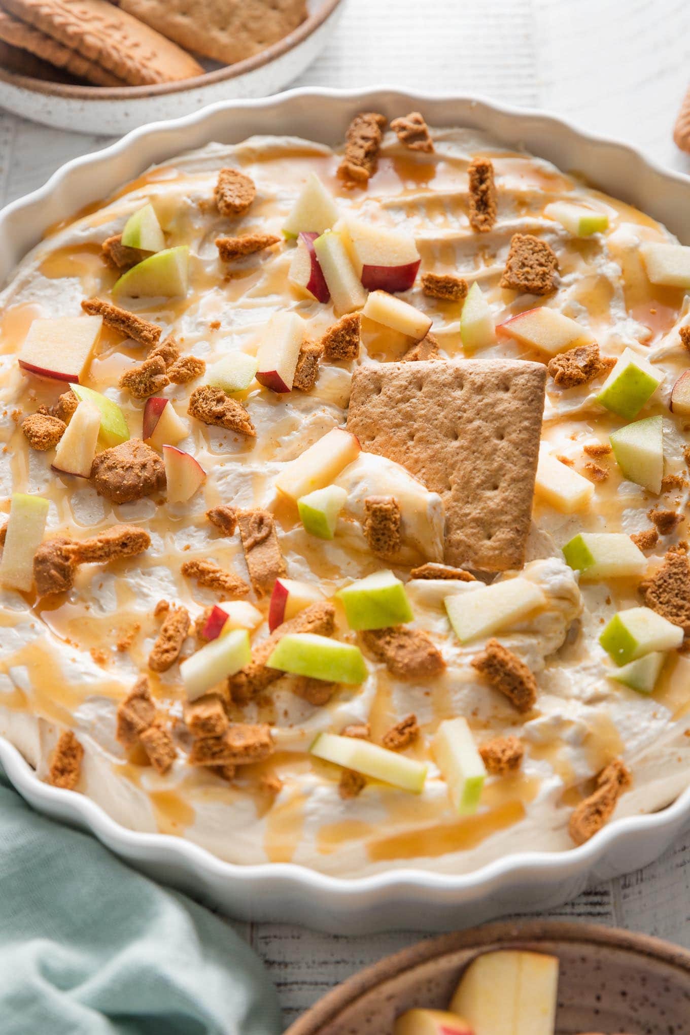 Large fluted serving dish full of creamy caramel apple cheesecake dip with a graham cracker being dipped in for a snack.